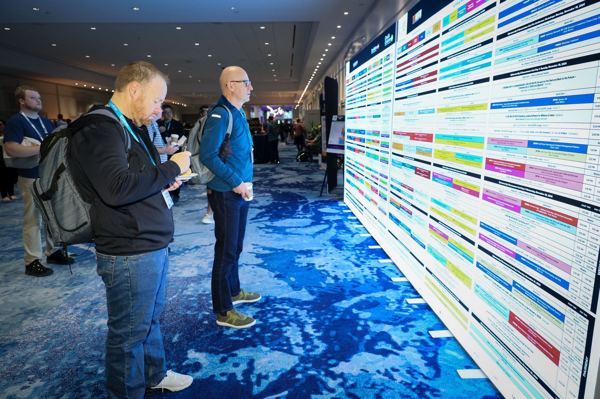 Two Live! 360 attendees standing in a hallway studying a large printed wall-sized session grid for the week.