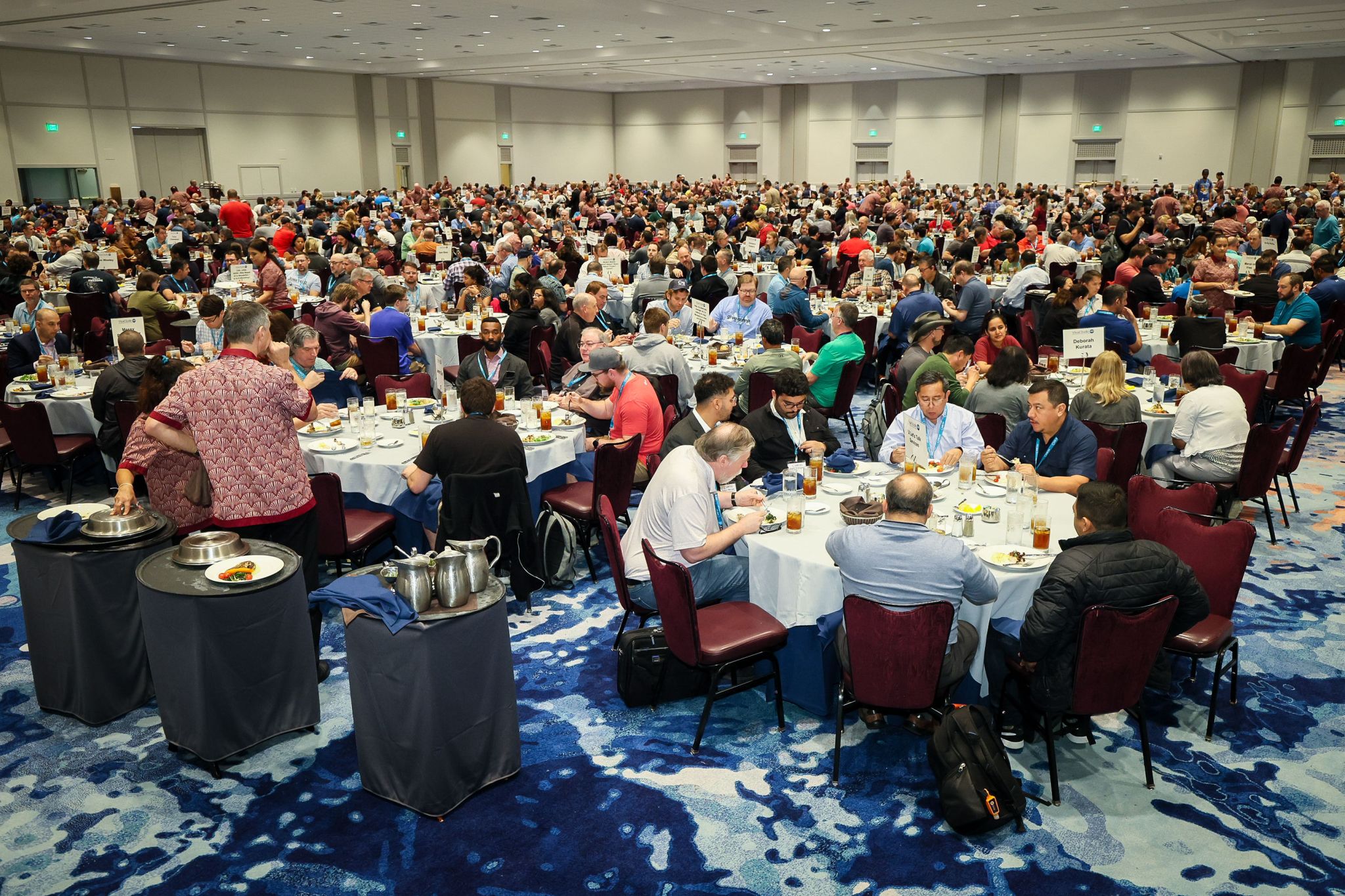 A large ballroom full of Live! 360 attendees eating lunch at round tables with printed topic signs on each table.